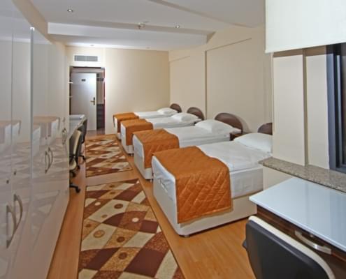 4-kisilik-kiz-ogrenci-yurdu 4 kiişilik kız öğrenci yurdu odasının pencere arkaya alınarak çekilen fotoğrafı. solda çalşma masası ve eşya dolapları, sağa 4 yatak ve çalışma masası