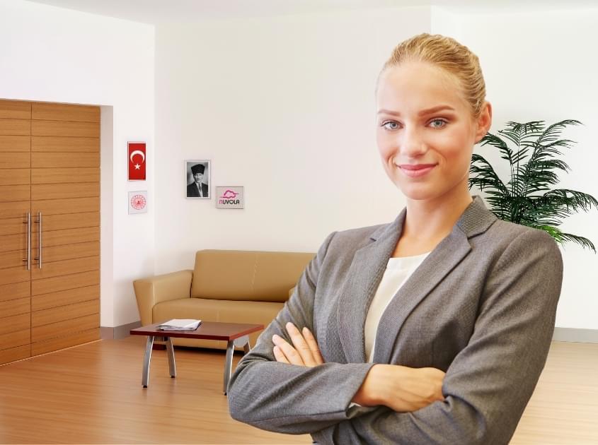 ellerini göğsünde birleştirmiş kadın, arkada misafir koltuğu, Atatürk portresi, Nuvola kız yurdu tablosu, Türk bayrağı ve bakanlık arması