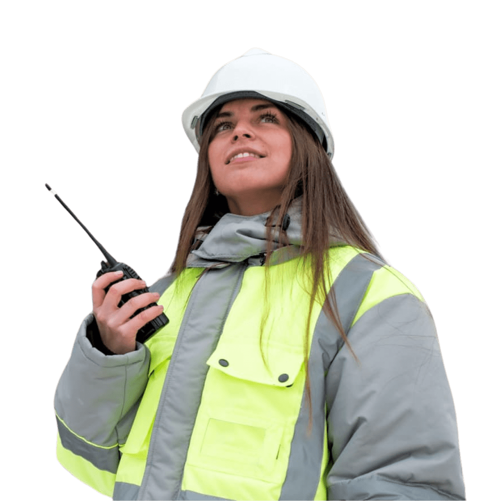 elinde telsiz tutan ve gülümseyen, kafasında baret olan, sarı yelek giymiş kadın mühendis