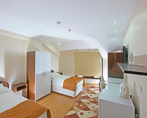 iki-kisilik-oda İki kişilik kız yurdu odasının giriş kapısı arkaya alınarak çekilen fotoğrafı. Solda iki adet yatak, eşya dolabı, komodin. Sağda buzdobı raf, televizyon ve eşya dolabı, karşıda stor perde ile kapatılmış pencere