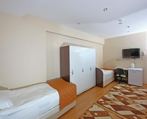 kiz-ogrenci-yurdu-3-kisilik-oda üç kişilik yurt odasının pencere tarafından çekilmiş fotoğrafı. solda iki yatak, eşya dolabı, çalışma masası, buzdolabı ve televiyzon. Karşıda giriş kapısı