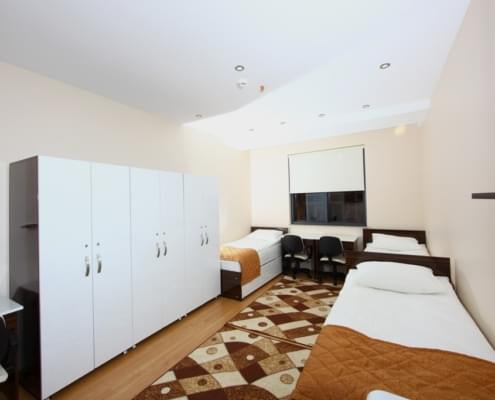 ogrenci-yurdu-dolap öğrenci yurdu odasının fotoğrafı. karşıda pencere ve çalışma masası, solda eşya dolapları ve odanın iki yanında yataklar