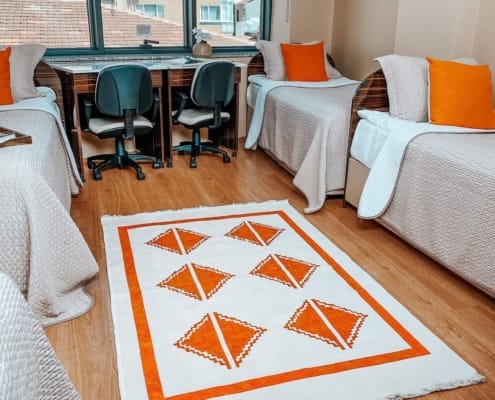 Nuvola Kız Öğrenci Yurdu Dört Kişilik Oda Nuvola Kız Öğrenci Yurdu 4 kişilik odasının karşıdan çekilmiş fotoğrafı. Görselde 4 yatak ve 2 çalışma masası yer alıyor. Görselde yer almayan ve kadraja girmemiş olan, buzdolabı ve televizyon diğer planda kalmış durumda.