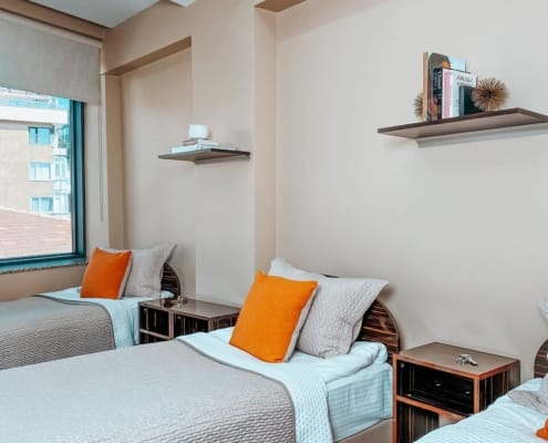 Nuvola Kız Yurdu, 3 kişilik oda seçeneği Nuvola Kız Yurdu, üç kişilik odasının profilden çekilmiş fotoğrafı. Üç yatak yanyana, yataklarda gri örtüler, bej yastık ve turuncu kırlent. Her yatağın yanında komodin bulunuyor.